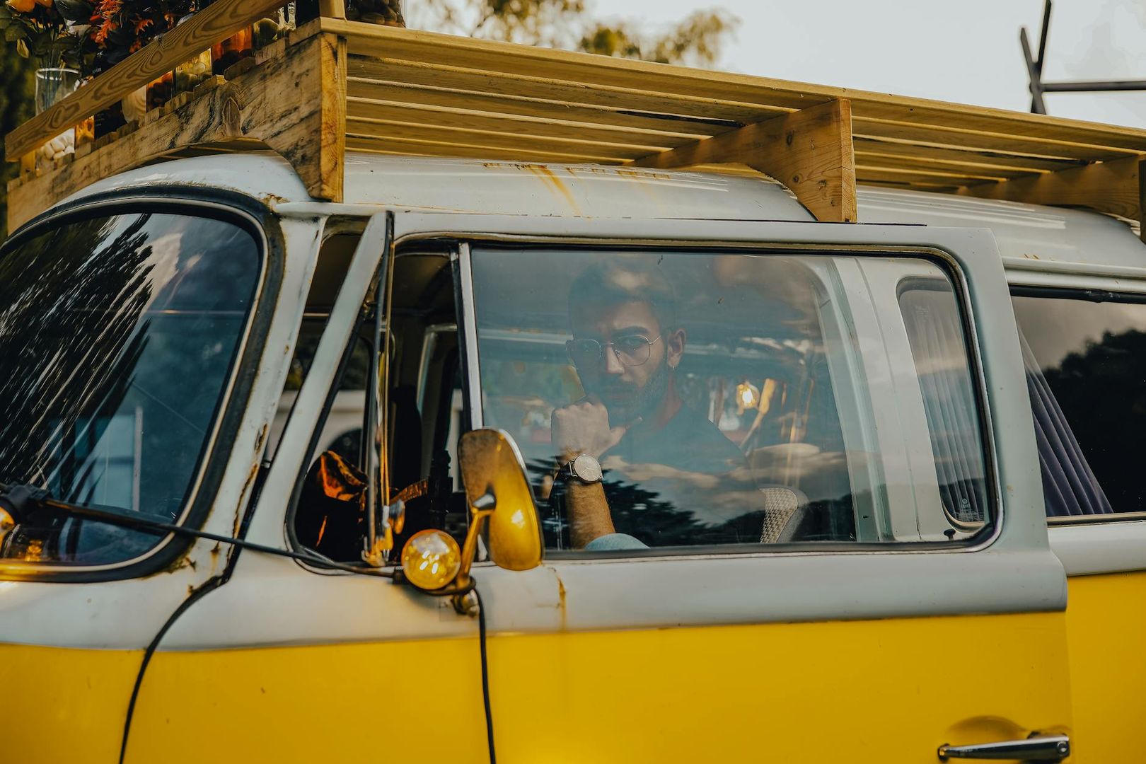 Homme dans un van aménagé jaune et blanc avec galerie de toit en bois.